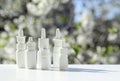 White dropper bottles, nose spray on background of spring flowering trees with copy space. Concept of allergy treatment. Nose