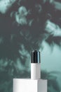 White dropper glass bottle with serum for skin care on the background of shadows of tree leaves