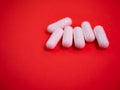 White drug capsules on colored red paper texture background. Macro close up pill medication. Big pharma. Off label approved Royalty Free Stock Photo