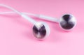 White Earphones lying on the pink background. Modern music concept. Audio technology. Close up photo