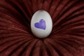 White egg with blue heart on a dark red pillow. Creative Easter background Royalty Free Stock Photo