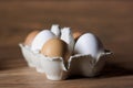 six pack white and beige eggs in a carton on a wooden board