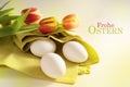 White eggs in a green napkin and red tulips, german text Frohe O