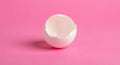 A white eggshell, cracked and half-open, is placed on a smooth pink surface. The Royalty Free Stock Photo