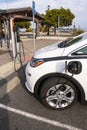 White electric car parked and getting a charge near a marina on an overcast day