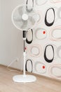 A white electric fan stands in a spacious room and cools the air.