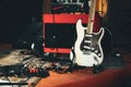 A white electric guitar and a red amplifier onstage with electrical audio cables and sound effects pedals