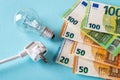 White electric plug, light bulb and euro money banknotes over blue background. Increasing of electricity cost