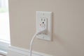 White GFCI electrical outlet with plugged in cord on beige wall Royalty Free Stock Photo