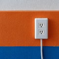 White electrical outlet with cord on a textured orange and blue wall Royalty Free Stock Photo