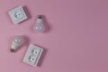 White electrical power sockets, light lamp bulbs on light pink background. Top view Royalty Free Stock Photo