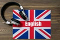 White electronic headphones lying on the flag of Great Britain with the text-English. Close-up, brown wooden background Royalty Free Stock Photo