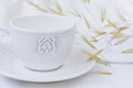 White elegant tea cup with saucer, dry plants, wild oats, white cotton fabric, styled image