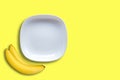 White empty ceramic plates and two bananas on yellow background Royalty Free Stock Photo