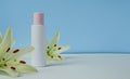 White empty cosmetic bottle with cream with pink cap, moisturizing lotion or shampoo framed with fresh lily flowers on a light Royalty Free Stock Photo