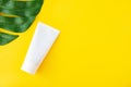 White empty cosmetic tube and green leaf of monstera on a yellow background. Spa care concept, branding mockup, top view Royalty Free Stock Photo