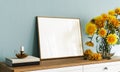 White empty mockup picture frame with yellow flowers on turquoise blue wall background Royalty Free Stock Photo