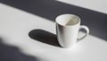 A white empty mug in bright sunlight creating a long shadow on a white background. Royalty Free Stock Photo