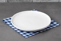 White empty plate on blue checkered napkin placed on gray surface in a kitchen setting during daytime Royalty Free Stock Photo