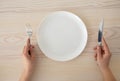 White empty plate and female hands holding silver fork and knife on wooden table background, top view Royalty Free Stock Photo