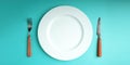 White Empty Plate with Fork and Knife Lay on Blue Table Background. Food Shortage, World Food Crisis Issue