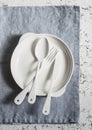 White enameled vintage cutlery and white ceramic plate on a blue linen napkin on a light background, top view.