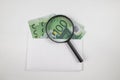 White envelope with a bunch of euro banknotes and a magnifier