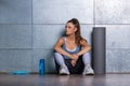 woman sitting on the floor arms rest on her spread legs looking to one site with ponytail mat and fitness equipment