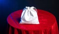 White Drawstring Pouch Centered on a Red Velvet Table with Blue Lighting fabric Royalty Free Stock Photo
