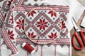 White fabric with red Ukrainian national embroidery in hoop, needle, scissors and thread on wooden table, flat lay Royalty Free Stock Photo