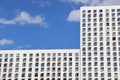 White facade of a modern tall building, dark windows and blue sky, bright light background Royalty Free Stock Photo