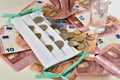 White facemask on top of euro bills and coins with finger counting coins. Royalty Free Stock Photo