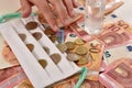 White facemask on top of euro bills and coins with fingers counting coins. Royalty Free Stock Photo