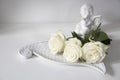 A white faience angel and bunch of roses are on the table