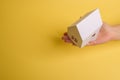 White family paper house in man hand on yellow background paper. Minimalistic style. Copy space. View from above. Horizontal Royalty Free Stock Photo