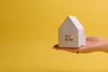 White family paper house in man hand on yellow background paper. Minimalistic style. Copy space. View from above. Horizontal Royalty Free Stock Photo