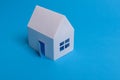 White family paper house over block of flats on blue background paper. Minimalistic and simple concept, style. Copy space. Royalty Free Stock Photo