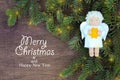 White felt Christmas angel with yellow star in hands to fresh natural branches of Christmas tree spruce on wooden background