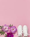 White female fashion sneakers and pink purple flowers peonies on pink background. Flat lay, top view, copy space. Women`s shoes.