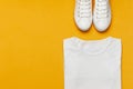 White female fashion sneakers, white T-shirt on yellow orange background. Flat lay top view copy space. Women`s shoes Royalty Free Stock Photo