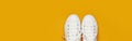 White female fashion sneakers on yellow orange background. Flat lay top view copy space. Women`s shoes. Stylish white sneakers.