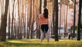 White female in a sports outfit from behind doing a neck stretch in a park among trees