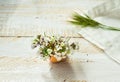 White field flowers in eggshell, napkin, green grass twig on wood surface in soft morning sunlight, Easter decoration