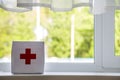 White first aid kit with red cross indoors on windowsill on blurred background. Healthcare concept