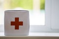 White first aid kit with red cross indoors on windowsill on blurred background. Healthcare concept