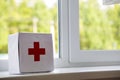 White first aid kit with red cross indoors on windowsill on blurred background. Healthcare concept