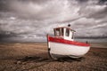 White fishing boat on the stony beach in Dungeness Beach, England, with a clouded sky in the back