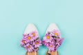 White flat female shoes filled with pink daisies and wildflowers on pastel blue background