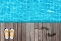 White flip flops, sandals and wet human footprint on wooden floor beside blue water in swimming pool at outside buildings from top