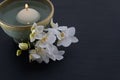 White floating candle in handmade ceramic bowl with a sprig of orchids on black slate board Royalty Free Stock Photo